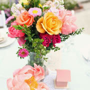 A table centre bouquet of orange, yellow, pink roses and white daisies